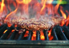Flames rise up around a burger cooking on a grill.