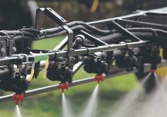 Close-up of the nozzles on a sprayer releasing chemical over a crop.