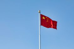 The flag of China flies atop a flagpole against a clear blue sky.