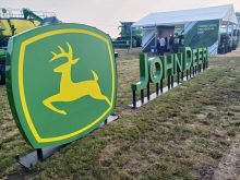 A photo of the John Deere green and yellow logo on a sign next to the words, "John Deere" at an unknown John Deere office location.