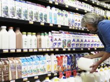 A woman looks at a jug of milk in front of a dairy display cooler in a grocery store.