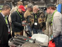 A man holds a drone in a booth at a trade show while others gather round to have a look.