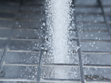 White fertilizer pellets fall through the metal bars of a screen designed to break up chunks.