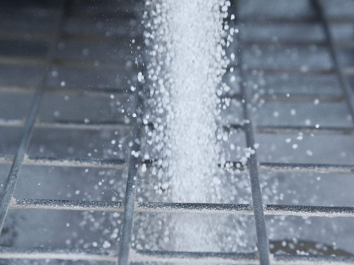 White fertilizer pellets fall through the metal bars of a screen designed to break up chunks.