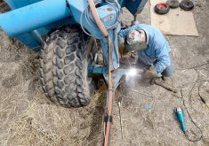 A man is welding on a piece of farm machinery.