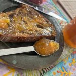 A piece of toast is generously coated with marmalade, and a spoonful of marmalade sits on the plate beside it.