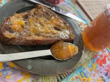 A piece of toast is generously coated with marmalade, and a spoonful of marmalade sits on the plate beside it.