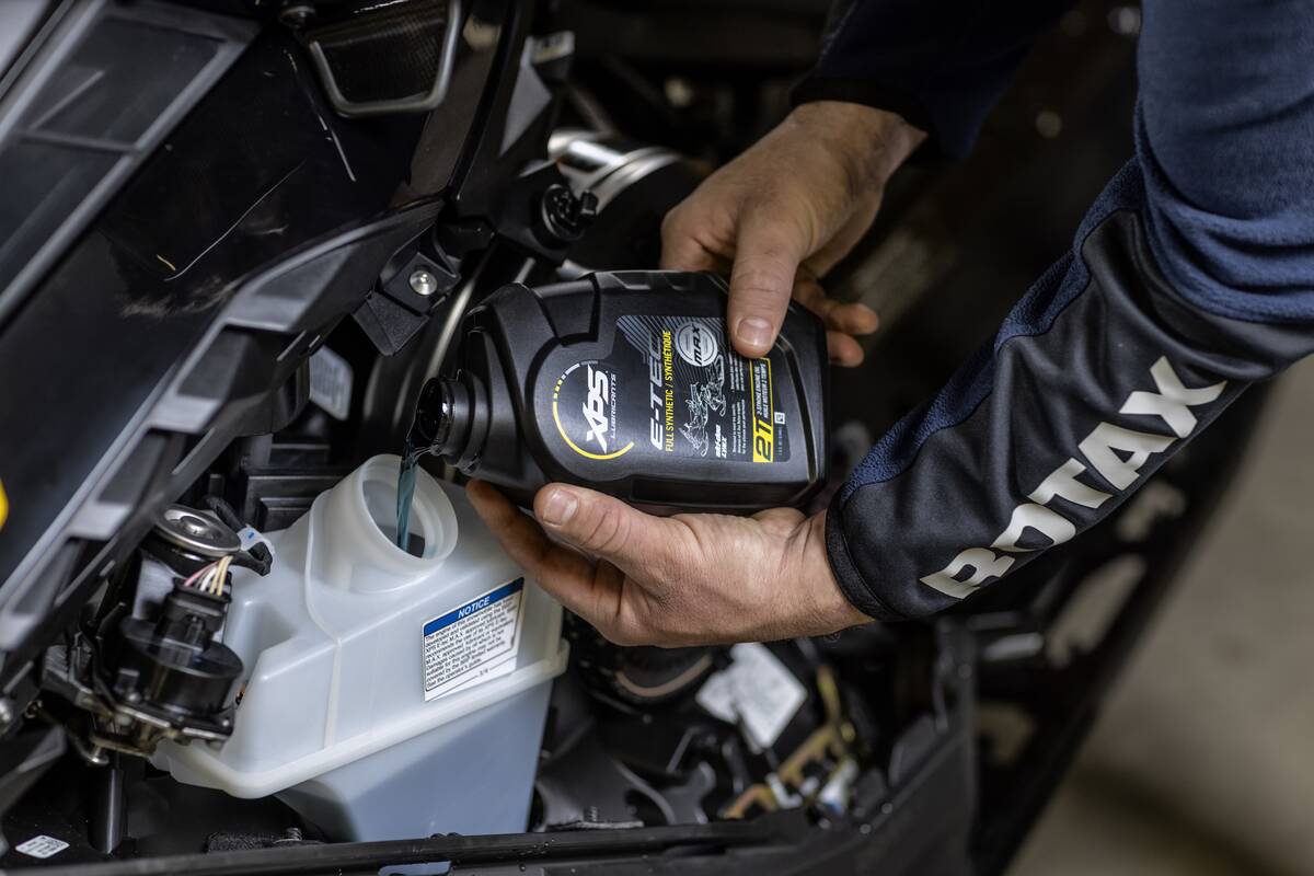 Close-up of a man's hands pouring oil into the reservoir on a snow machine.