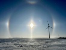 A perfect circle is scribed in the crisp blue sky by the sun and its sun dogs with a giant wind turbine in the foreground on a bitterly cold day.