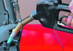 A gas nozzle is seen pumping fuel into a red tractor.