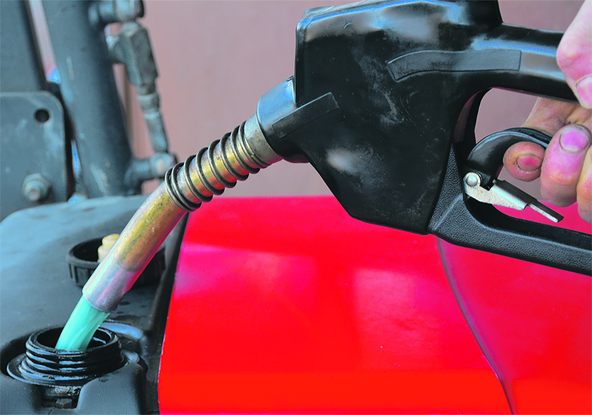 A gas nozzle is seen pumping fuel into a red tractor.
